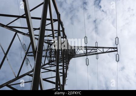 Enorme pilone alto ad alta tensione fotografato lateralmente dal basso verso l'alto con le linee ad alta tensione del braccio laterale e gli isolatori contro il cielo blu wi Foto Stock