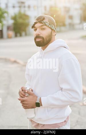 Ritratto di uomo giovane sportivo e sicuro con foulard sulla testa in piedi con bottiglia d'acqua al mattino Foto Stock