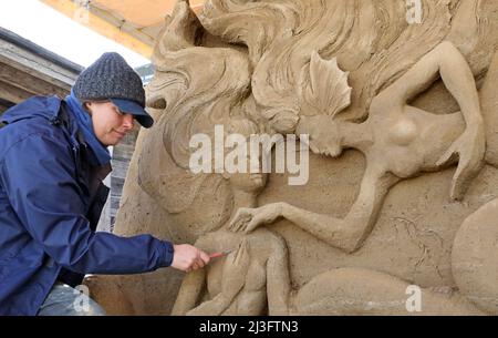 08 aprile 2022, Meclemburgo-Pomerania occidentale, Warnemünde: Nella mostra di scultura di sabbia 'Warnemünde Sand World' Susanne Ruseler (Paesi Bassi) lavora sulla sua scultura 'la Sirenetta'. Quattro artisti provenienti da quattro paesi trasformano 300 tonnellate di sabbia in uno spettacolo all'aperto sul tema delle "fiabe del mare". L'apertura è il 11.04.2022. Foto: Bernd Wüstneck/dpa Foto Stock