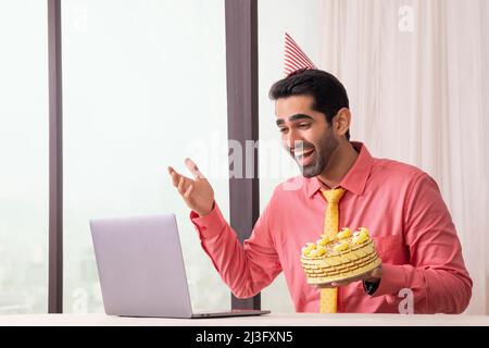 Felice uomo d'affari che festeggia il compleanno con la videochiamata che chiacchiera con gli amici in ufficio Foto Stock