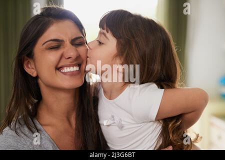 E un grande kissy per Mummy. Scatto di una bambina che dà alla madre un bacio sulla guancia a casa. Foto Stock