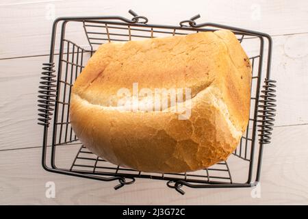 Una pagnotta di pane aromatico di grano in un cestino fatto di filo, su un tavolo di legno, primo piano, vista dall'alto. Foto Stock