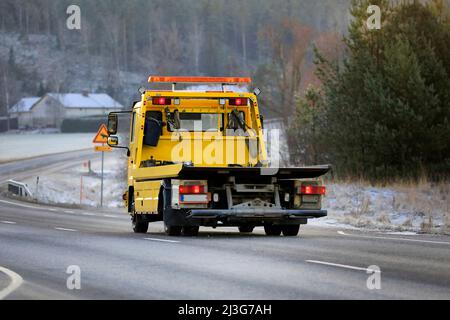 Carro attrezzi a pianale giallo a velocità elevata su strada in una giornata invernale, vista posteriore. Foto Stock