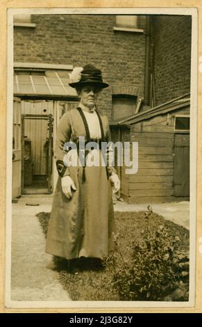 Scheda originale del gabinetto dell'epoca edoardiana, donna anziana che guarda poppa, forse una zia o una nonna, che indossa un cappello con una piuma in esso e guanti bianchi, al di fuori della sua casa urbana nel giardino, Crouch End, Nord. Londra, Regno Unito circa 1905. Foto Stock