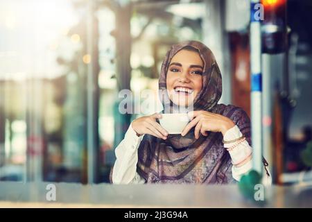 Il caffè è la mia delizia pomeridiana. Ritratto di una giovane donna che ha una tazza di caffè in un caffè. Foto Stock