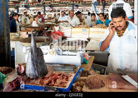 Dubai. EMIRATI ARABI UNITI. Il mercato del pesce. Fishmonger che vende pesce spada, parlando a un telefono cellulare Foto Stock