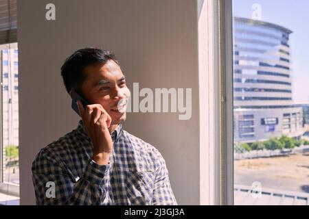 Un primo piano di un uomo d'affari al telefono sorridente, accanto alla vista della città Foto Stock