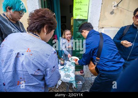 Portogallo, Lisbona, quartiere di Alfama, vecchia donna che vende a un gruppo di turisti asiatici un tipico liquore di gusto Ginja Ginjinha jininha alcoho ciliegia sulla strada Foto Stock