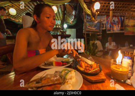 Filippine, Palawan, El Nido, giovane filippina donna gode di un pasto di pesce in salsa in un ristorante turistico, a lume di candela Foto Stock