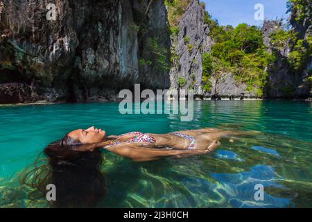 Filippine, Palawan, El Nido, Arcipelago Bacuit, Isola di Miniloc, Piccola Laguna, una giovane filippina che indossa un bikini che rievatte la pittura di John Everett Millais, Ophelia, in acque turchesi e ambiente tropicale, circondata da scogliere carsiche Foto Stock