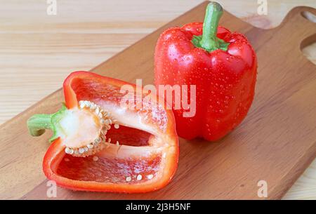 Peperoni rossi con gocce d'acqua su tagliere di legno Foto Stock