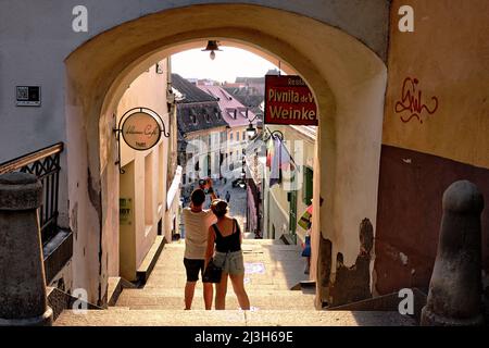 SIBIU, ROMANIA - 30 LUGLIO 2018: Un paio di turisti scattano una foto con smartphone dall'arco di strada medievale della città vecchia Foto Stock