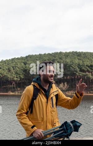 Un ragazzo con un impermeabile giallo che si erge di fronte al lago. Ha la sedia da campo in mano. Egli avrà un riposo presso il lago. Parco naturale in un autunno d'oro Foto Stock