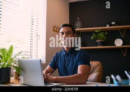 Un giovane uomo d'affari asiatico siede al suo ufficio e sorride Foto Stock