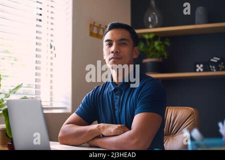 Un giovane asiatico siede alla sua scrivania con le braccia piegate Foto Stock