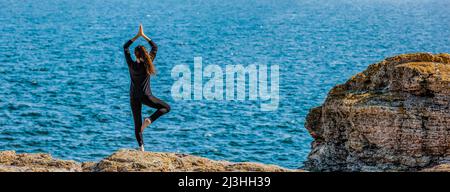 Donna che fa esercizio di yoga su una costa Foto Stock