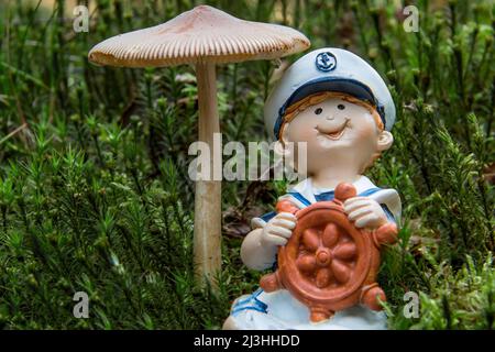 Raccoglitrice di funghi - una figura marinara si siede sotto un fungo nella foresta Foto Stock