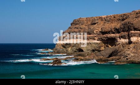 Spagna, Isole Canarie, Fuerteventura, costa occidentale, El Puertito de los Molinos, vista del mare blu-verde e costa rocciosa dove si incontra il surf, azzurro cielo e nuvoloso Foto Stock