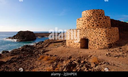 Spagna, Isole Canarie, Fuerteventura, costa occidentale, Punta de Toston, torre angolare a tre livelli a destra del quadro, mare e rocce e surf a sinistra, cielo blu, poche nuvole bianche Foto Stock