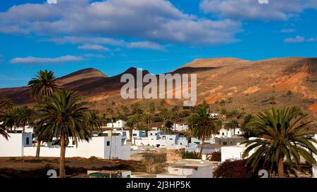 Isole Canarie, Lanzarote, isola vulcanica, a nord dell'isola, città oasi, Haria, vista delle case di Haria e dietro di loro colline vulcaniche aride, palme, azzurro cielo con nuvole bianche Foto Stock