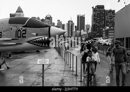 12 Av/W 46 Street, New York City, NY, USA, Una famiglia cammina presso il Fighter Vought F-8K Crusader con base portaerei sul ponte superiore dell'Intrepid Sea, Air & Space Museum - un museo di storia militare e marittima americano espone la portaerei USS Intrepid. Foto Stock