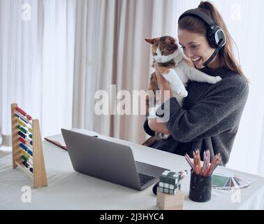 Non si può mai dire dove si ferma la vostra influenza. Scatto di un insegnante giovane che mostra il suo gatto a uno studente online a casa. Foto Stock