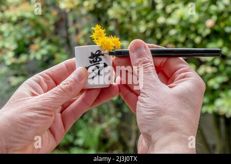 Un uomo scrive la parola sogno in giapponese su una tazza bianca con fiori gialli all'interno Foto Stock