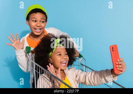 Ritratto di piccoli amici trendy amicizia cavalcare carrello prendendo selfie registrazione video avendo divertimento isolato su sfondo di colore blu brillante Foto Stock