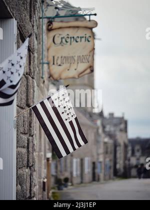 La bandiera bretone a un crêperie in Locronan nel dipartimento del Finistère in Bretagna. I cottage sono stati costruiti in granito e risalgono al 17th secolo. L'ambientazione storica di Locronan è stata presentata in molte produzioni cinematografiche e televisive. Locronan è una destinazione popolare per le escursioni. Foto Stock