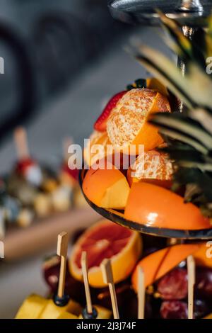 Assortimento di frutta tropicale su un piatto bianco con succo fresco, sfondo tessile grigio. Vista dall'alto. Foto Stock