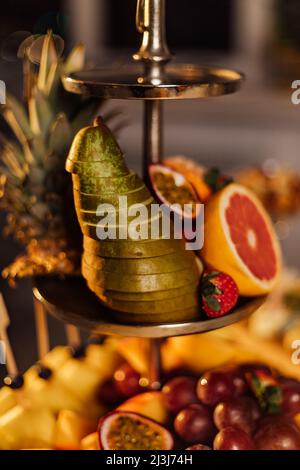 Assortimento di frutta tropicale su un piatto bianco con succo fresco, sfondo tessile grigio. Vista dall'alto. Foto Stock