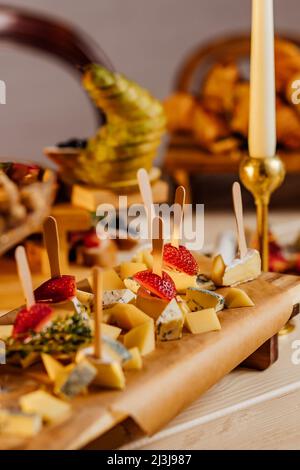 Piatto di formaggi con diversi formaggi, uva, noci, miele, pane e datteri su sfondo rustico in legno. Selezione di varietà di formaggio in stile retrò al buio Foto Stock