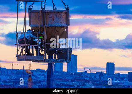 Vienna, cantiere di alta casa di appartamenti, gru, secchio di cemento o benna di gru, cementazione, operaio di costruzioni, progetto 'Danube Flats', skyline di Vienna, fiery tramonto nel distretto 22. Donaustadt, Austria Foto Stock