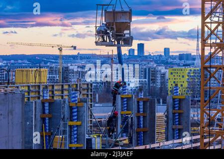 Vienna, cantiere di alta casa di appartamenti, gru, secchio di cemento o benna di gru, cementazione, operaio di costruzioni, progetto 'Danube Flats', skyline di Vienna, fiery tramonto nel distretto 22. Donaustadt, Austria Foto Stock