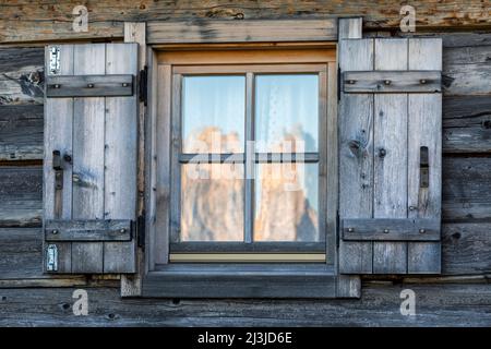 Italia, Alto Adige / Südtirol, Castelrotto / Kastelruth, Alpe di Siusi / alpe di Siusi - la finestra di una capanna, sul vetro il riflesso dello Sciliar / montagna dello Sciliar all'alba Foto Stock