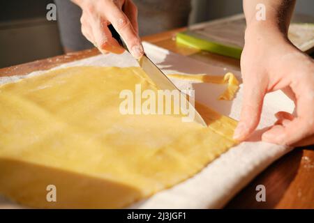 Chiudere le mani della donna, tagliando l'impasto alla luce del sole sul tavolo Foto Stock