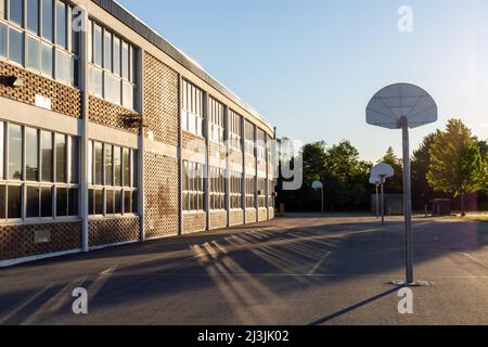 Cortile con campo da basket e edificio scolastico esterno in serata di sole Foto Stock