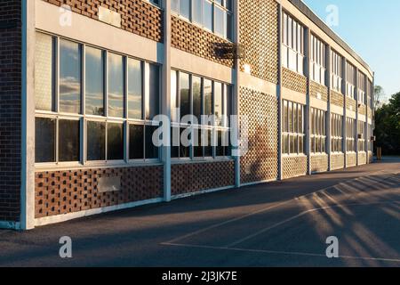 Edificio scolastico e cortile scolastico in serata con il sole che si riflette nelle finestre della struttura Foto Stock