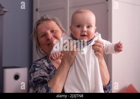 Nonna anziana che tiene un bambino di 7 mesi nelle sue braccia a casa Foto Stock