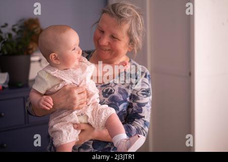 Nonna anziana che tiene un bambino di 7 mesi nelle sue braccia a casa Foto Stock