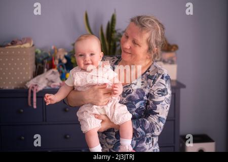 Nonna anziana che tiene un bambino di 7 mesi nelle sue braccia a casa Foto Stock