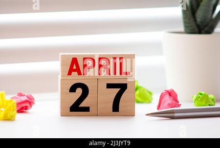 Concetto di evento promemoria del calendario. Cubetti di legno con numeri e mese il 27 aprile con luce solare Foto Stock