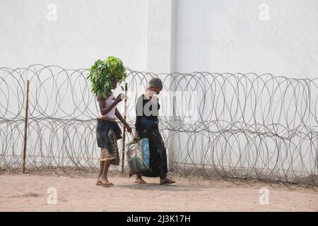 Le donne congolesi passano davanti a un filo rasoio che protegge un edificio delle Nazioni Unite; Kinshasa, Repubblica Democratica del Congo. Foto Stock