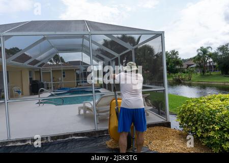 L'uomo discarica carriola piena di ghiaia intorno alla piscina in Florida Foto Stock