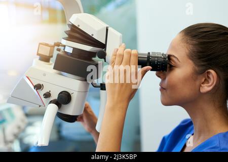 Uno sguardo più da vicino. Shot di un giovane patologo che guarda i campioni al microscopio. Foto Stock
