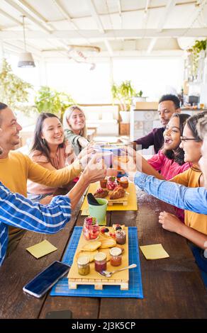 Foto verticale di persone multiculturali che hanno la prima colazione bere caffè e Grazie. Buon divertimento comunitario in un bar con terrazza. Divertente gruppo di Foto Stock