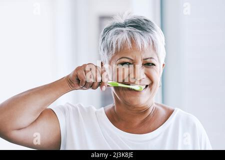 Le prime ore del mattino. Ritratto di una donna matura e allegra che gli spazzolava i denti mentre guardava la fotocamera a casa. Foto Stock