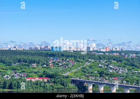 Kemerovo, Russia - 24 giugno 2021. Case di villaggio suburbano sulla riva e edifici residenziali a più piani dietro una foresta su una collina, in primo piano a r Foto Stock