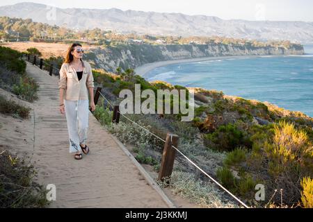 Una giovane donna cammina su un sentiero sopra la spiaggia a Point Dume. Foto Stock