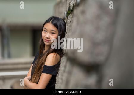 Ritratto di una ragazzina che si appoggia contro un muro di pietra; Hong Kong, Cina Foto Stock